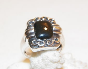 May include: A silver ring with a black gemstone set in a decorative, ornate design.