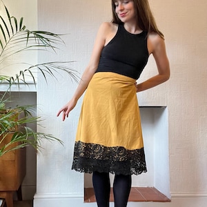 May include: A mustard yellow wrap skirt with a black lace trim. The skirt is knee-length and has a simple, elegant design.