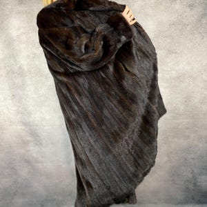 May include: A full-length, dark brown fur coat with a textured, vertical pattern. The coat appears to be made of luxurious fur and has a classic design. The coat is being held up, showcasing its length and texture.