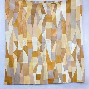 May include: A large wall hanging made of leather patchwork in shades of brown, beige, and cream. The leather pieces are cut into geometric shapes and sewn together to create a unique and abstract design.