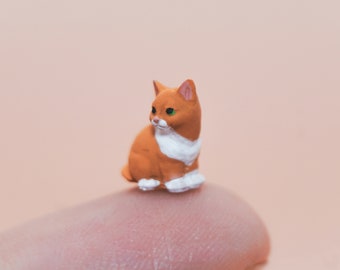 May include: A small orange and white cat figurine with green eyes. The figurine is sitting on a finger.