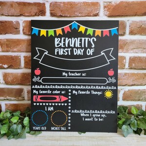 May include: A black chalkboard with a colorful banner at the top that says "Bennett's First Day Of". The chalkboard has spaces to fill in information about the child's first day of school, including their teacher's name, favorite color, favorite things, age, and height.