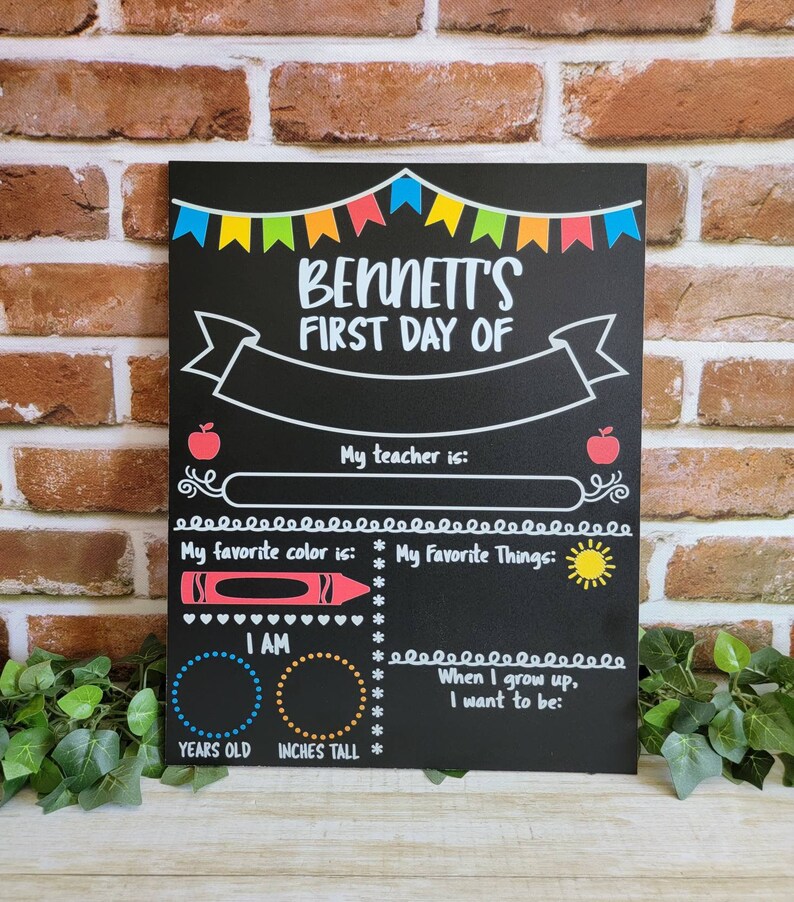May include: A black chalkboard with a colorful banner at the top that says "Bennett's First Day Of". The chalkboard has spaces to fill in information about the child's first day of school, including their teacher's name, favorite color, favorite things, age, and height.