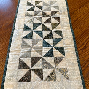 May include: A white table runner with a teal border and a geometric pattern of gray and teal triangles.