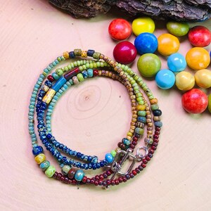 May include: Multi-strand beaded necklace with a silver clasp. The necklace features a variety of colors, including red, blue, green, and brown.