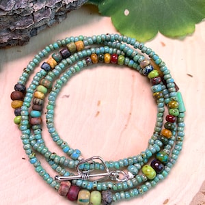 May include: A multi-strand necklace made of turquoise blue, brown, green, yellow, and red beads. The necklace has a silver clasp.