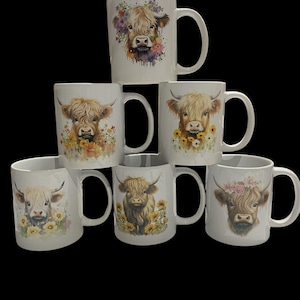 Op de afbeelding: Zes witte keramische mokken met verschillende Highland Cow-ontwerpen. Elke mok heeft een ander ontwerp met een koe met bloemmotieven. De koeien zijn bruin en wit met zwarte neuzen.