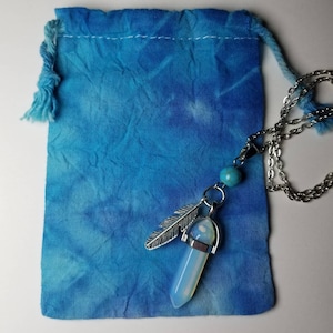 May include: A blue tie-dye drawstring bag with a silver necklace featuring a white opal crystal pendant, a silver feather charm, and a turquoise bead.