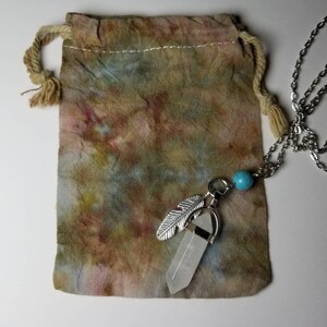 May include: A white crystal pendant with a silver feather charm hangs from a silver chain. The pendant is in a small, brown fabric bag with a drawstring.