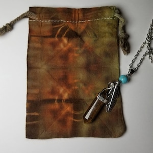 May include: A brown and green tie-dye drawstring bag with a silver necklace featuring a brown tiger's eye crystal pendant, a silver feather charm, and a turquoise bead.