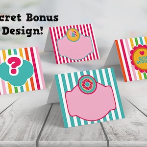 May include: Four printable Girl Scout cookie themed table cards with colorful stripes and a pink background. The cards feature a question mark, a donut, a Girl Scout logo, and a blank space for text.