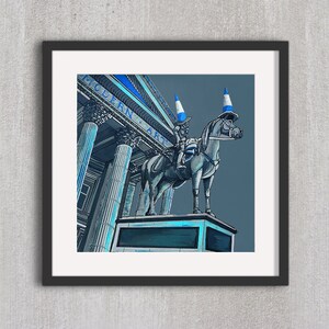 May include: A framed art print featuring a whimsical illustration of a statue of a horse and rider, both adorned with traffic cones. The background shows a building with the words "MODERN ART" in blue. The artwork is set against a gray backdrop.