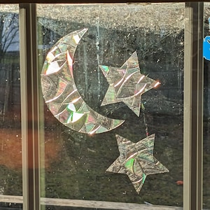 Könnte beinhalten: Ein Fenster mit einem Halbmond und zwei Sternen aus schimmerndem, mosaikartigem Material. Mond und Sterne sind am Fenster befestigt.