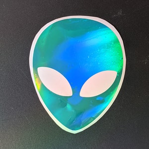 May include: A holographic sticker of an alien head with white eyes. The sticker is green, blue, and iridescent.