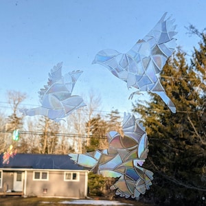 May include: Three iridescent stained glass bird decals on a window. The birds are facing different directions and are made of small, colorful pieces of glass.