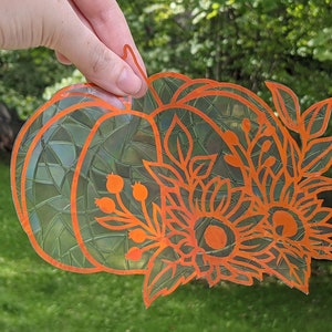 Peut inclure: Autocollant en vinyle orange représentant une citrouille avec un motif de tournesol et de feuilles. L'autocollant a un effet de vitrail.