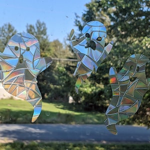 May include: Three iridescent ghost window clings with a stained glass pattern. The ghosts are white with a rainbow sheen.