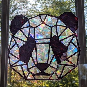 May include: A geometric panda face made from iridescent, holographic material. The panda is black and white with a geometric design.