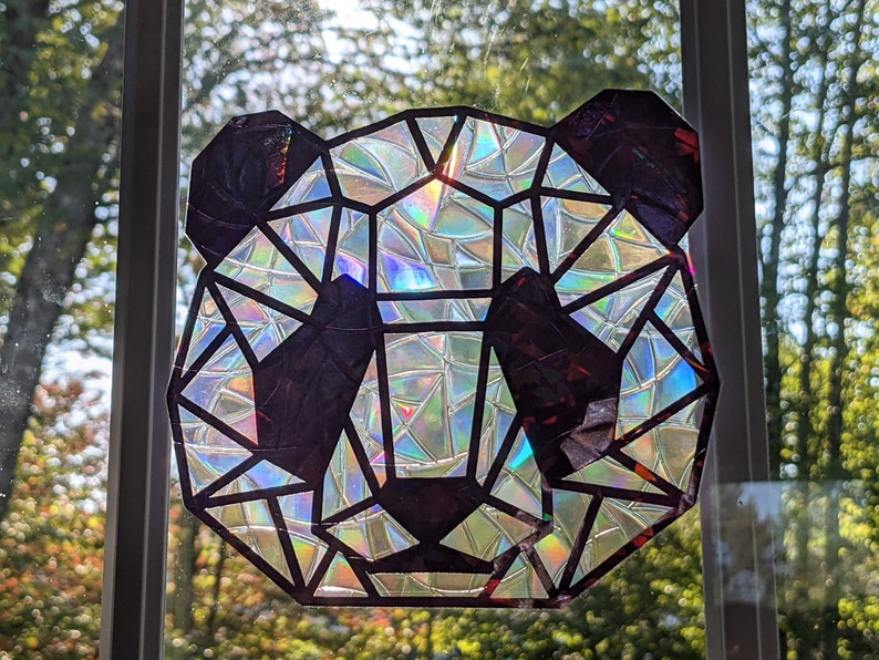 May include: A geometric panda face made from iridescent, holographic material. The panda is black and white with a geometric design.
