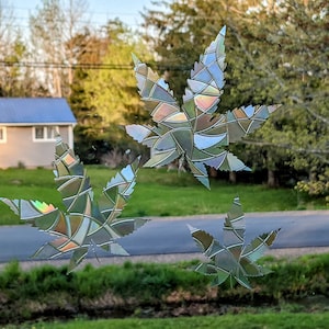 Puede incluir: Tres pegatinas de vinilo holográficas iridiscentes con forma de hojas de marihuana. Las hojas son de estilo vitral con una variedad de colores y formas.