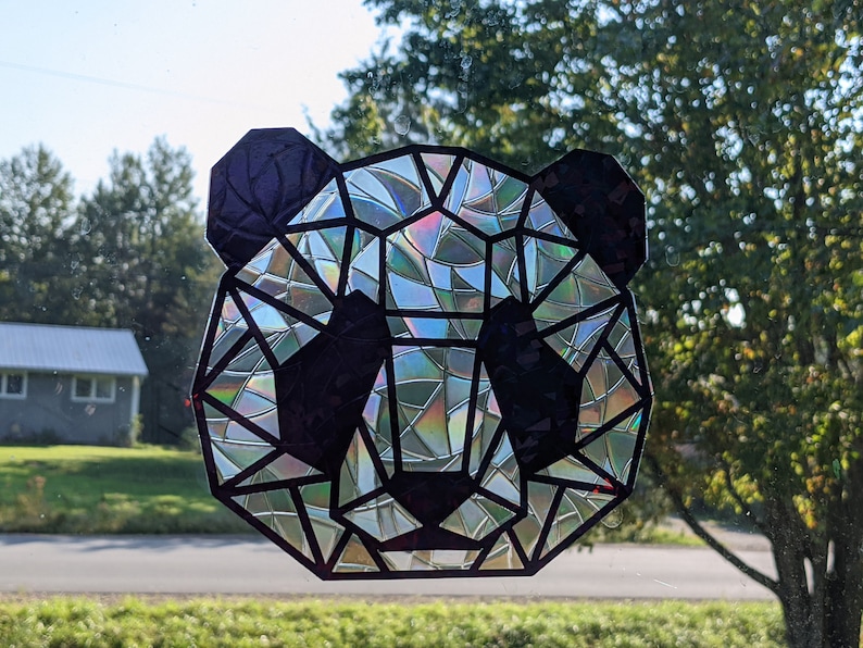 May include: A geometric panda face sticker with a iridescent finish. The sticker is made of black vinyl with a holographic design.
