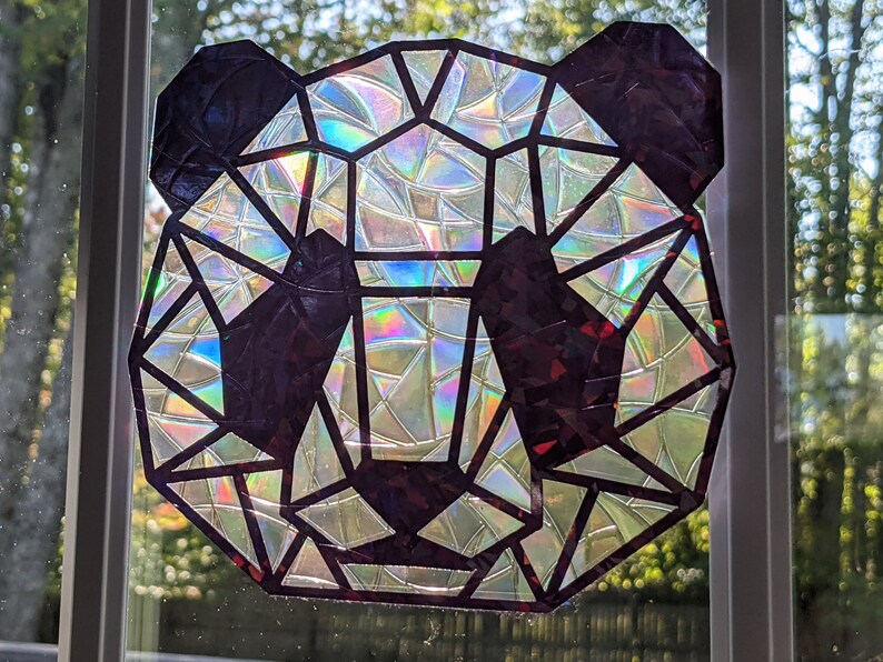 May include: A geometric panda bear design made of iridescent, holographic paper. The panda is outlined in black and the background is white.