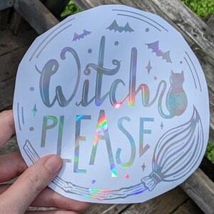 May include: A round, white holographic sticker with the words "Witch PLEASE" in a whimsical font. The sticker features illustrations of bats, stars, a cat, and a broom, all in a similar holographic finish. The design is perfect for Halloween.