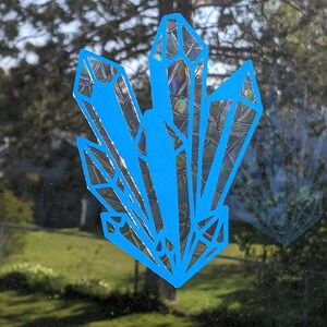 Op de afbeelding: Een blauwe kristalsticker met een holografische afwerking. De sticker heeft de vorm van een cluster kristallen.
