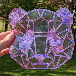 May include: A pink iridescent geometric bear-shaped sticker with a holographic finish.