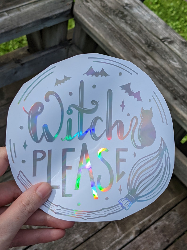 May include: A round, holographic sticker with the words "Witch Please" in a script font. The design includes bats, a cat, a broom, and stars. The sticker has a shiny, iridescent finish.
