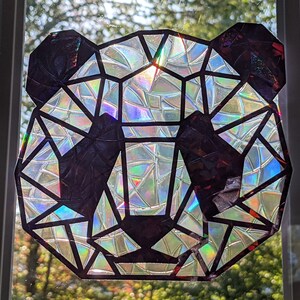 May include: A geometric panda face made from iridescent, holographic paper. The panda is black and white with a geometric design.