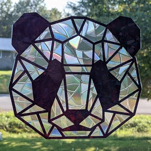 May include: A geometric panda face sticker with a iridescent finish. The sticker is black and has a geometric design with a rainbow effect.