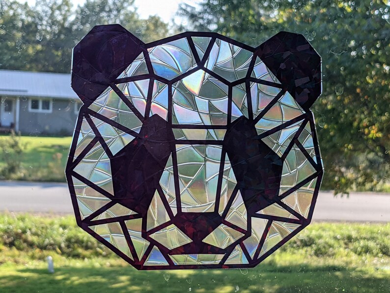 May include: A geometric panda face sticker with a iridescent finish. The sticker is black and has a geometric design with a rainbow effect.
