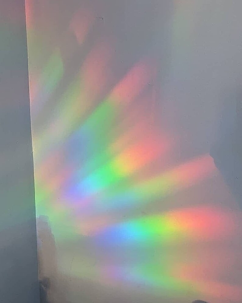 May include: A white wall with a rainbow prism light reflecting on it. The light is a spectrum of colors, including red, orange, yellow, green, blue, indigo, and violet.