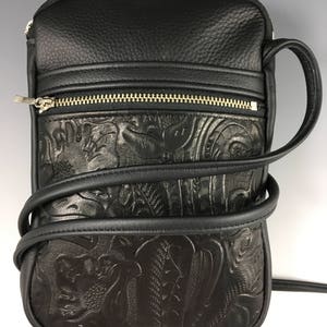 May include: Black leather crossbody bag with an embossed floral design. The bag has a zipped pocket on the front and a long adjustable strap.