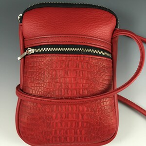May include: A red leather crossbody bag with a crocodile embossed pattern and a black zipper. The bag has a long strap and a small pocket on the front.
