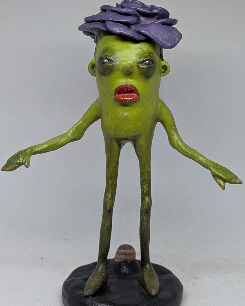 May include: A quirky sculpture of a humanoid figure. It has a green body, red lips, and a purple flower-like headpiece. The figure stands on a black base with arms outstretched. The sculpture is hand-painted.
