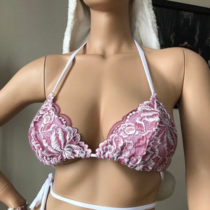 Puede incluir: Top de bikini de encaje malva y blanco con cuello halter y cierre de lazo. Las copas triangulares tienen un ribete de encaje festoneado. El bikini se muestra en un maniquí.
