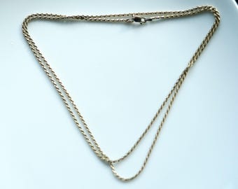 May include: A gold-colored rope chain necklace. The necklace is made of twisted metal strands and has a clasp closure. The chain is displayed on a white surface.