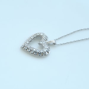 May include: A silver necklace with a heart-shaped pendant encrusted with small, clear gemstones.