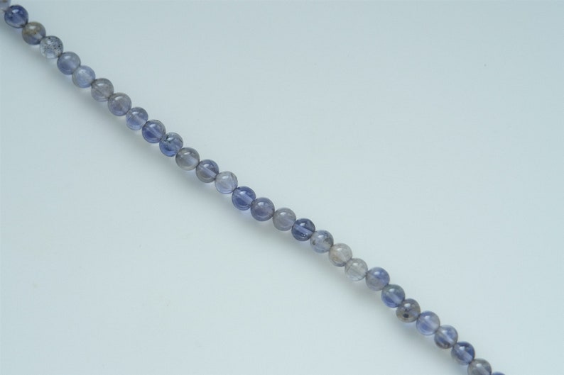 May include: A strand of round, light blue and gray gemstone beads.