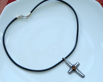 May include: A black leather cord necklace with a silver cross pendant. The cross has a brown stone in the center and is decorated with small silver beads.