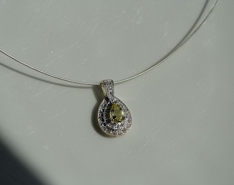 May include: A silver necklace with a pear-shaped pendant featuring a yellow gemstone surrounded by smaller clear gemstones.