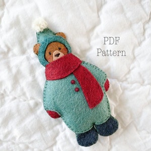 Felt Christmas Ornament. Felt Bear Ornament. Felt Christmas Bear Ornament on a white background. The bear is wearing a green felt snowsuit with a red felt scarf. The text says PDF Pattern. It is a Christmas sewing pattern.