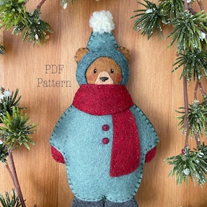 A felt christmas ornament bear dressed in a green snowsuit with red scarf. Text reads PDF pattern. Whimsical christmas ornament pattern. Felt ornament pattern. Christmas sewing pattern. Winter sewing project. Cute bear pattern.