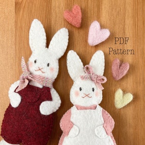 Two white felt rabbit ornaments. Bunny ornaments in red overalls and pink dress. Text reads PDF pattern. A valentine sewing pattern. Felt valentine ornaments. Felt ornament pattern.