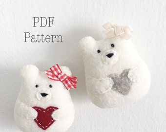 May include: Two white felt polar bear ornaments holding red and gray felt hearts. The bears are wearing red and white gingham and white satin bows.