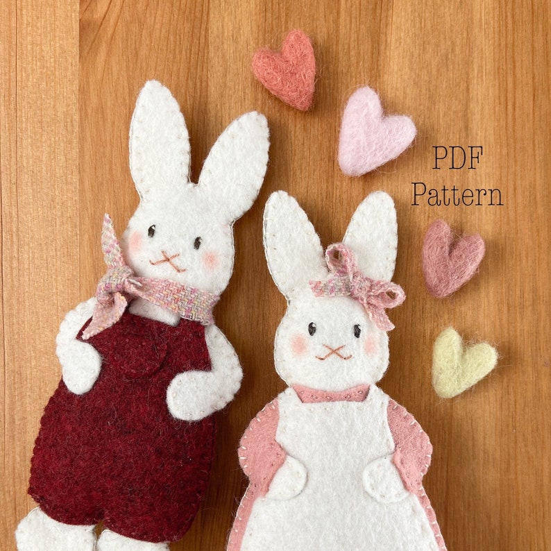 Two white felt rabbit ornaments. Bunny ornaments in red overalls and pink dress. Text reads PDF pattern. A valentine sewing pattern. Felt valentine ornaments. Felt ornament pattern.