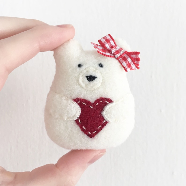 Hand holding felt bear ornament. Christmas ornament pattern. Valentine ornament pattern. Felt ornament pattern. A small felt white bear holding a red heart. Christmas sewing patterns.