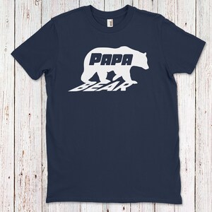 Puede incluir: Una camiseta azul marino con una silueta blanca de un oso con las palabras "Papa Bear" dentro del oso.